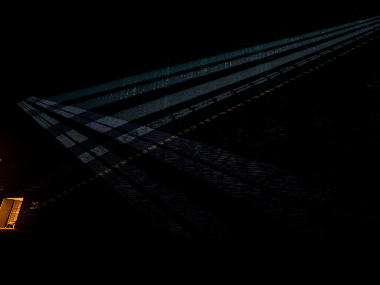 Projected light beams across a dark building facade